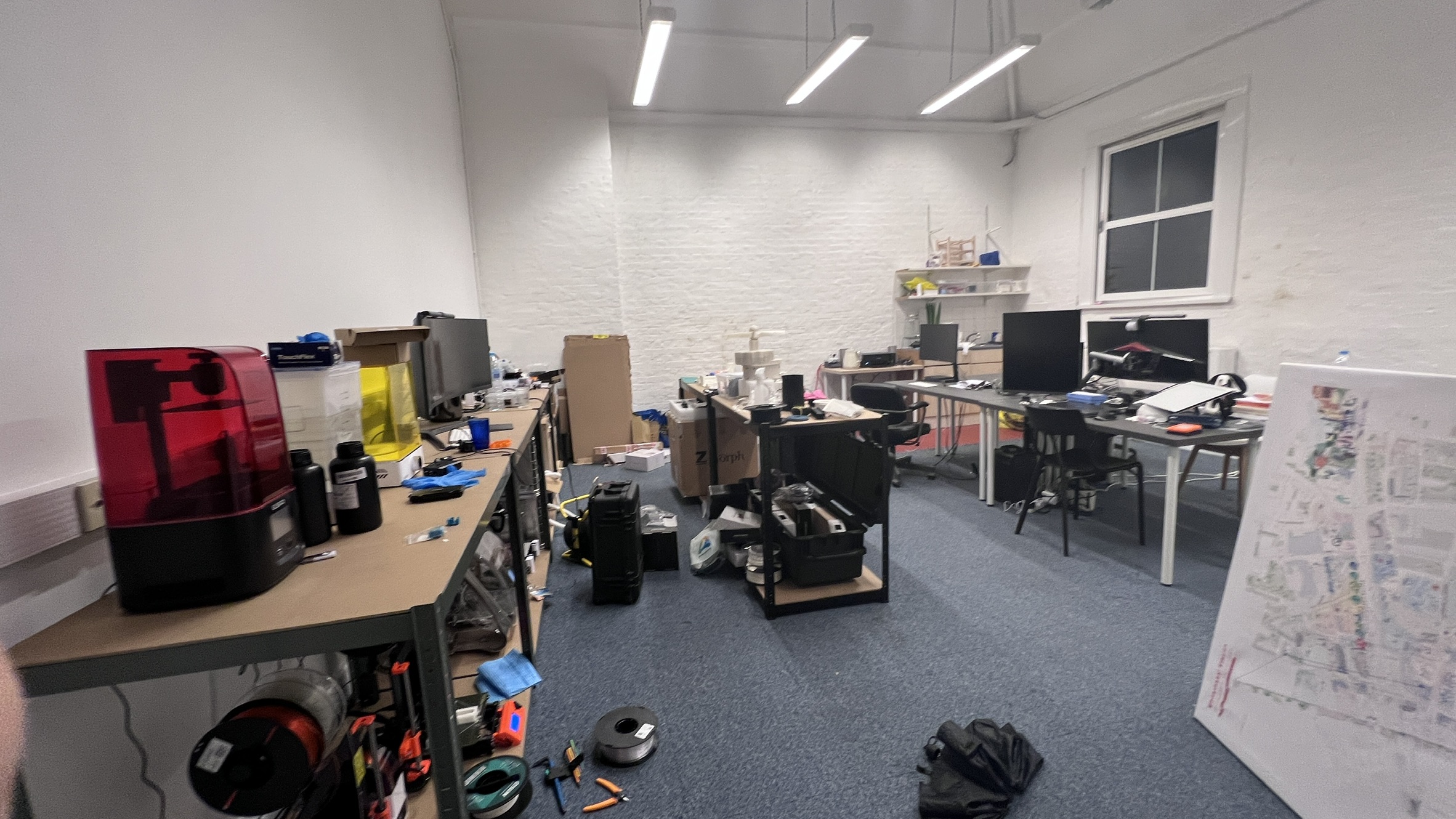 The studio at peak operation — resin printer running in the foreground, Zmorph multi-tool in the middle, three workstations along the back wall, filament racks below. Real working state, not a staged shot.