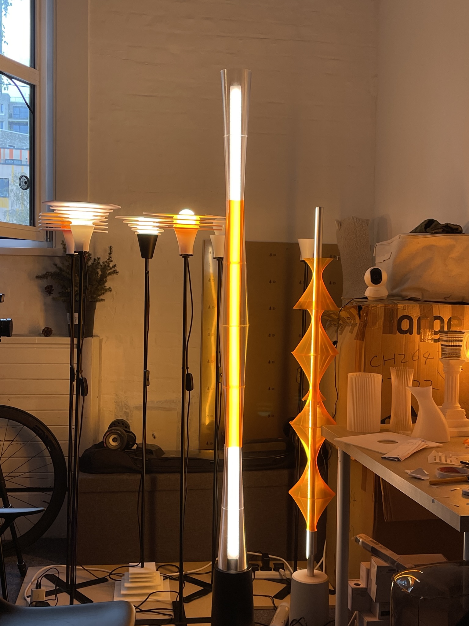 Lamp shade designs lit at night in the studio — pillar lamp shade (FDM, spiral-vase mode) and diamond-stack tower (SLA). Lamp bases and electronics sourced; shades designed and fabricated in-house.