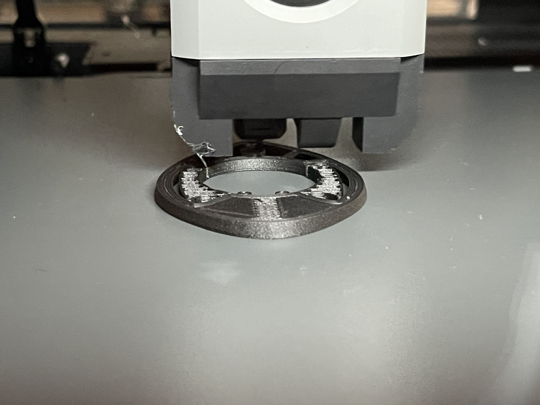 FDM print head laying down a black structural ring with internal lattice — process shot of an in-progress production part