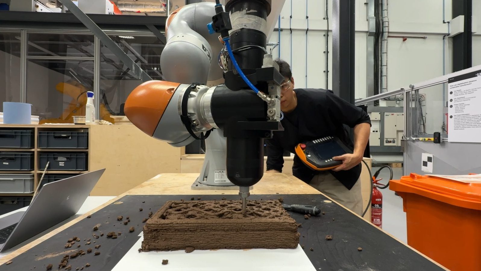 KUKA LBR iiwa mid-print — robotic arm extruding a clay brick with the custom pneumatic end effector